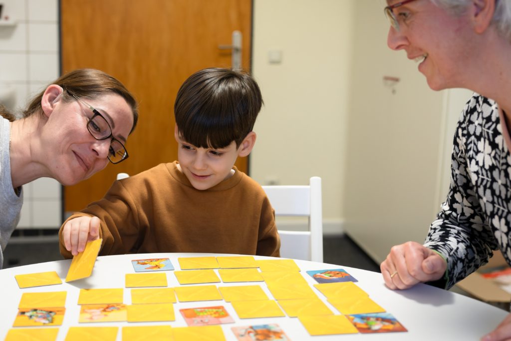 Ein kleiner Junge, seine Mutter und eine Pädagogin spielen mit Memory-Karten.