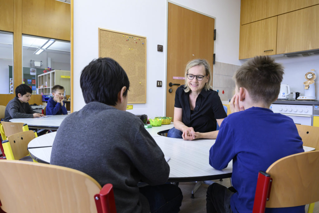 Zwei Jungen sitzen mit einer blonden Frau an einem runden Tisch und lesen gemeinsam Brailleschrift.