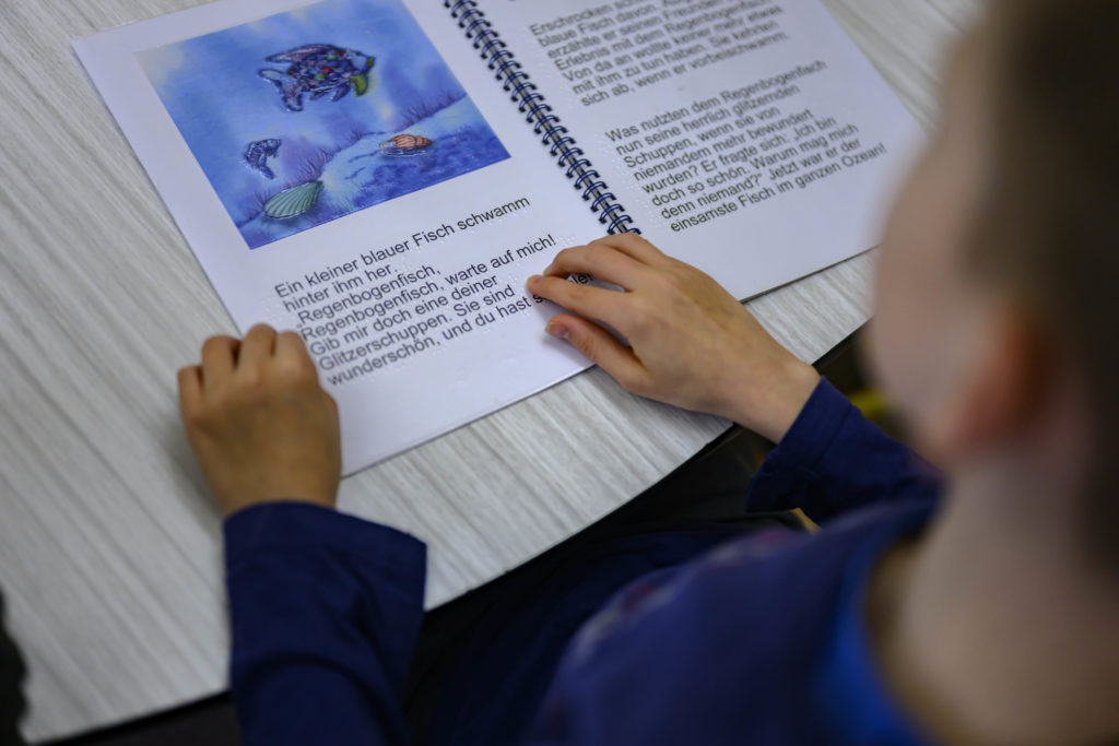 Ein Schüler fährt mit seinen Händen über ein Buch, das sowohl in schwarzer, als auch in Brailleschrift geschrieben ist.
