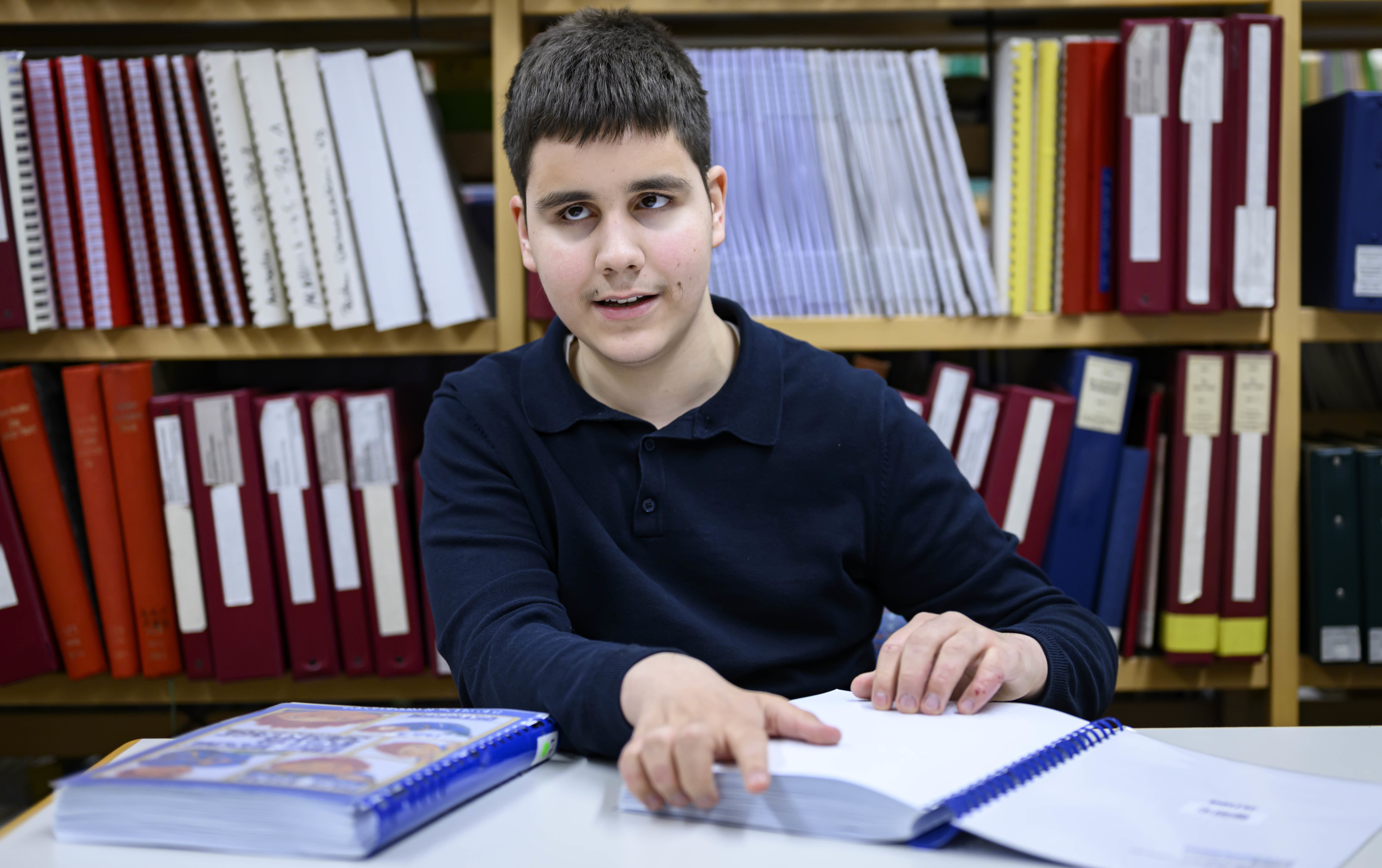 Ein Junge mit schwarzem Haar fährt mit den Fingern über ein Buch in Brailleschrift.