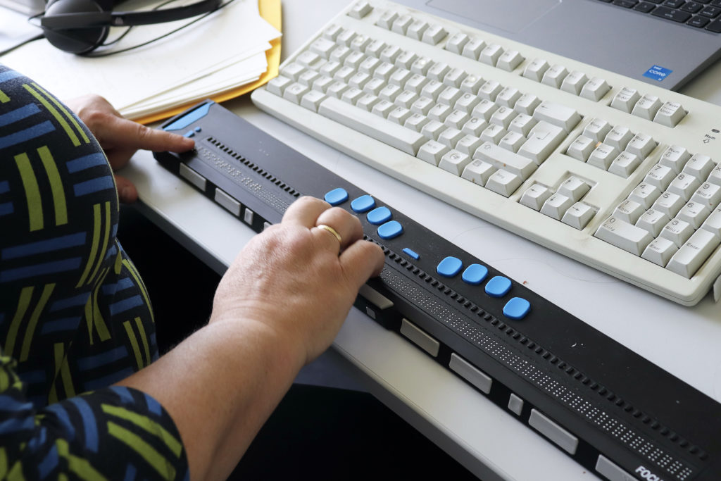 Zwei Hände sind auf einer Brailletastatur aufgelegt. Oben im Bild liegt die Standard-Tastatur.