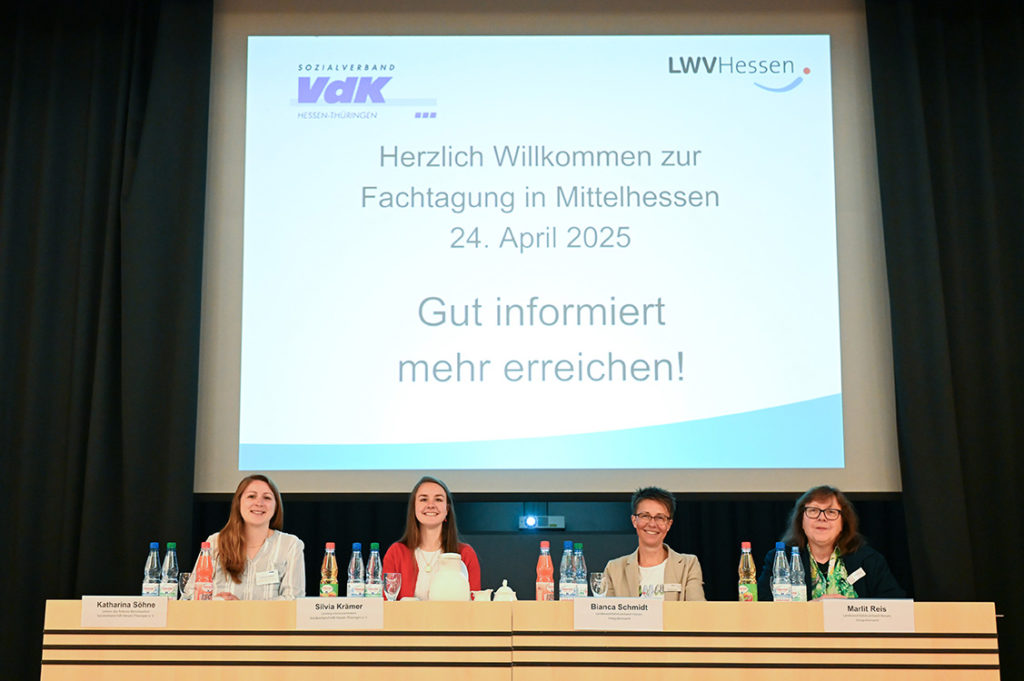 Vor einer groß projizierten Begrüßungsfolie sitzen vier Vertreterinnen der Veranstalter: Katharina Söhne, Silvia Krämer Bianca Schmidt, Marlit Reis
