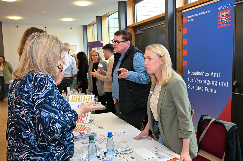 Zwei Frauen und zwei Männer stehen erklärend hinter dem Stand des hessischen Versorgungsamtes, davor zwei interessierte Personen