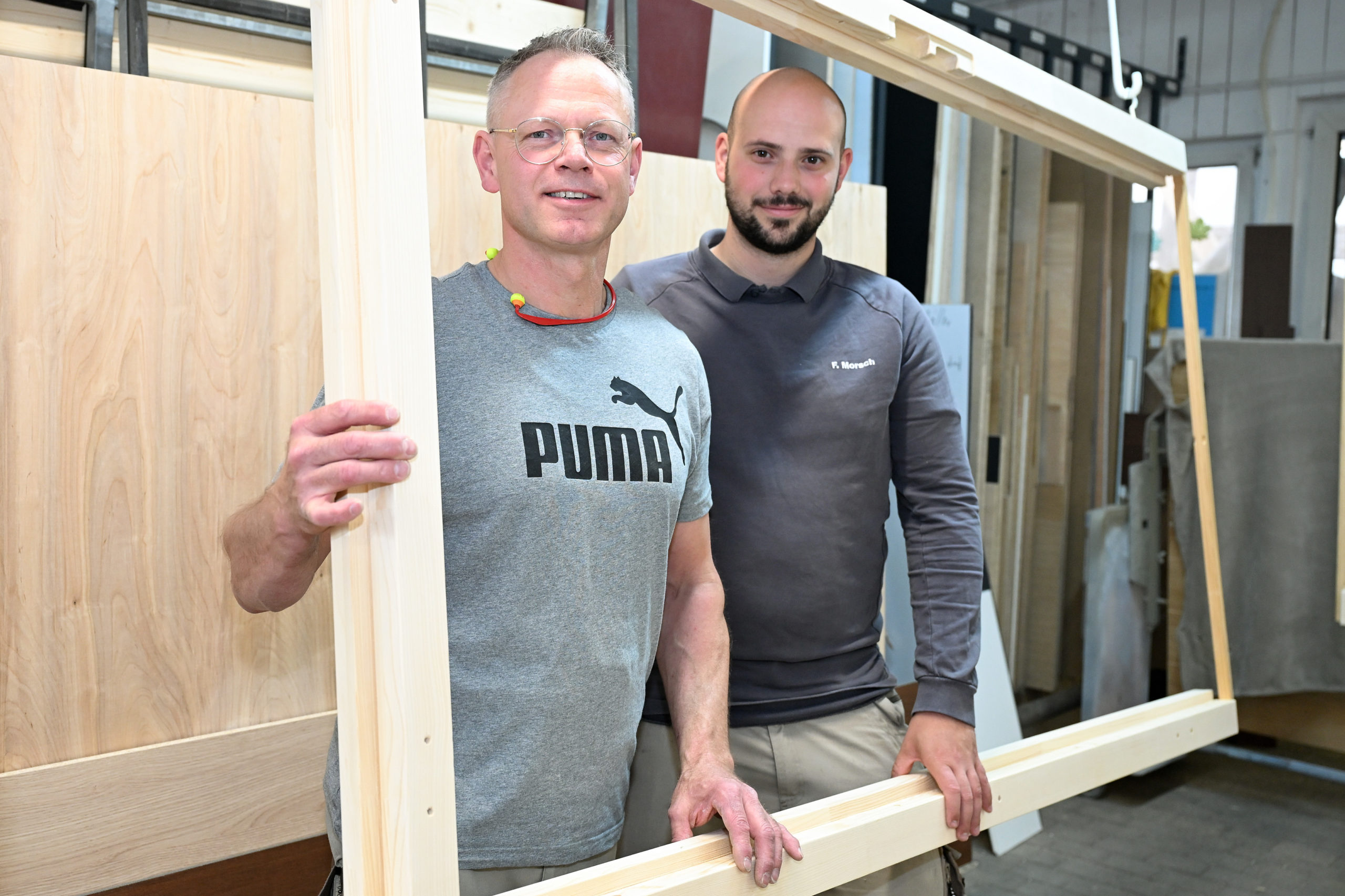 Thorsten Werner und Juniorchef Felix Morsch posieren in der Tischlerei-Werkstatt in einem Fensterrahmen