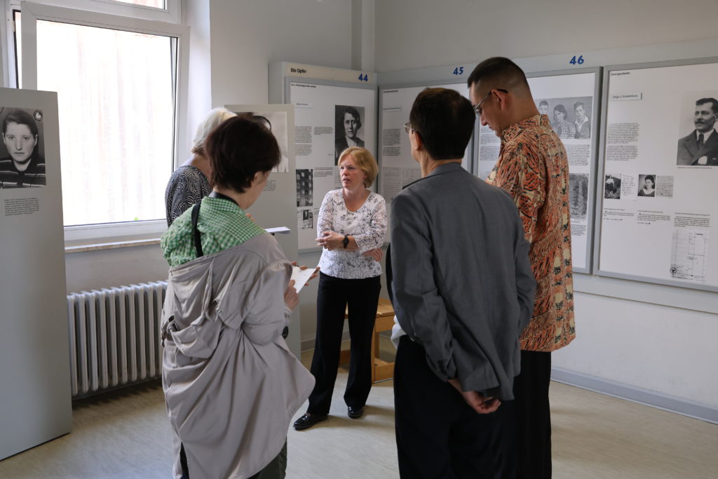 Die Besucher stehen im Halbkreis um eine Person mit rötlichen Haaren, die ihnen die Ausstellung schildert.