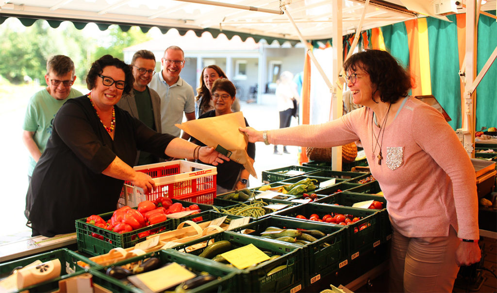 Eine Frau bedient eine andere Frau an einem Marktstand. Beide lachen.