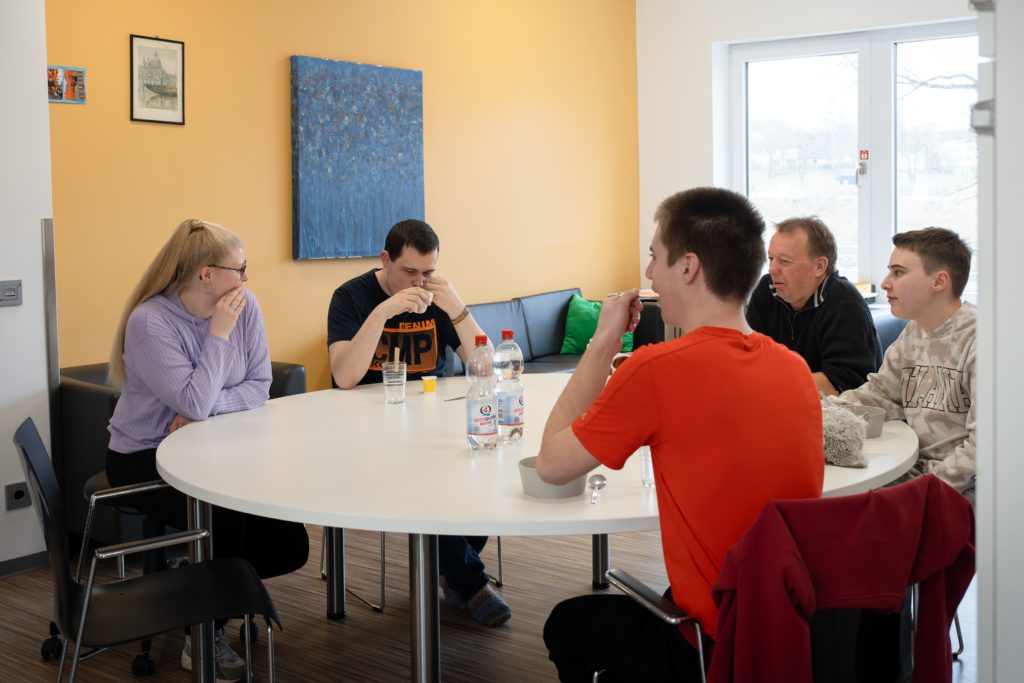 Eine Gruppe Menschen sitzt an einem runden Tisch und unterhält sich.