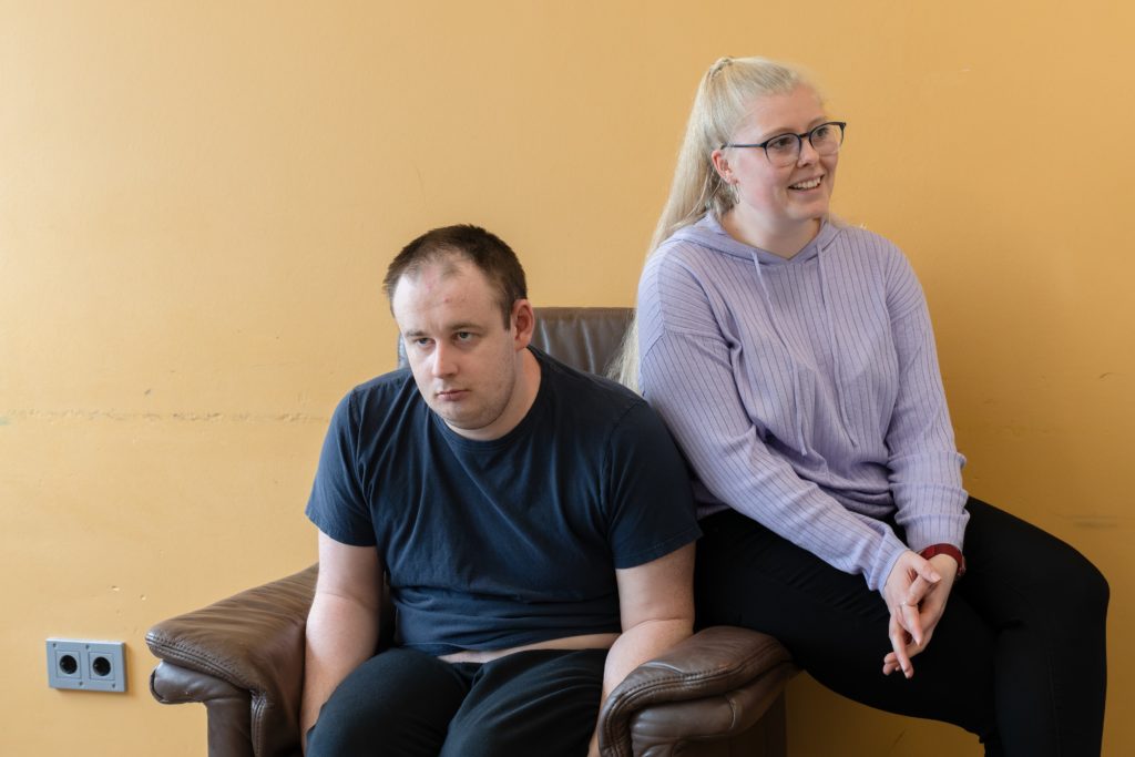Ein Mann und eine blonde Frau sitzen auf einem Ledersessel. Die blonde Frau lacht herzlich.