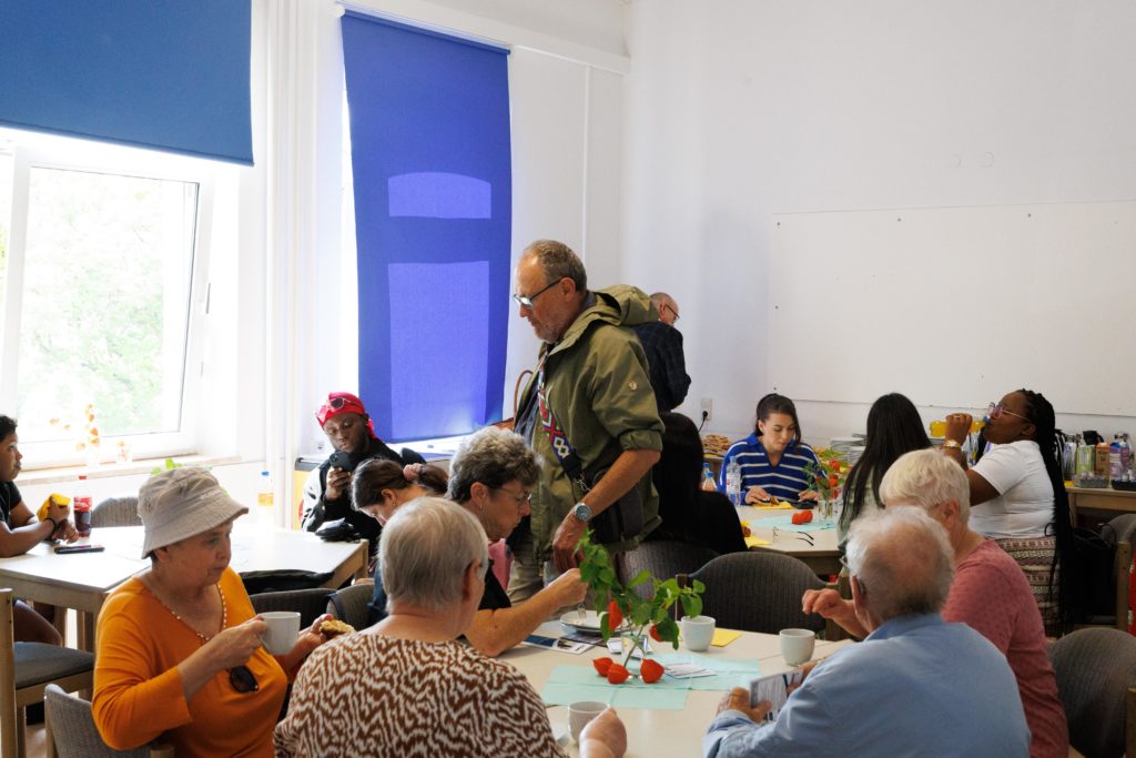 Einige Besucher sitzen in einem hellen Aufenthaltsraum an mehreren runden Tischen und diskutieren bei Kaffee das Gesehene.