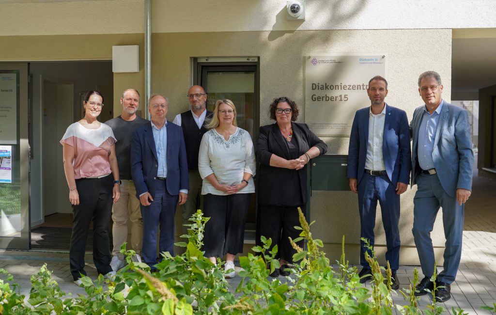 Die Projektbeteiligten stehen vor dem Eingang der Einrichtung und schauen zufrieden in die Kamera.