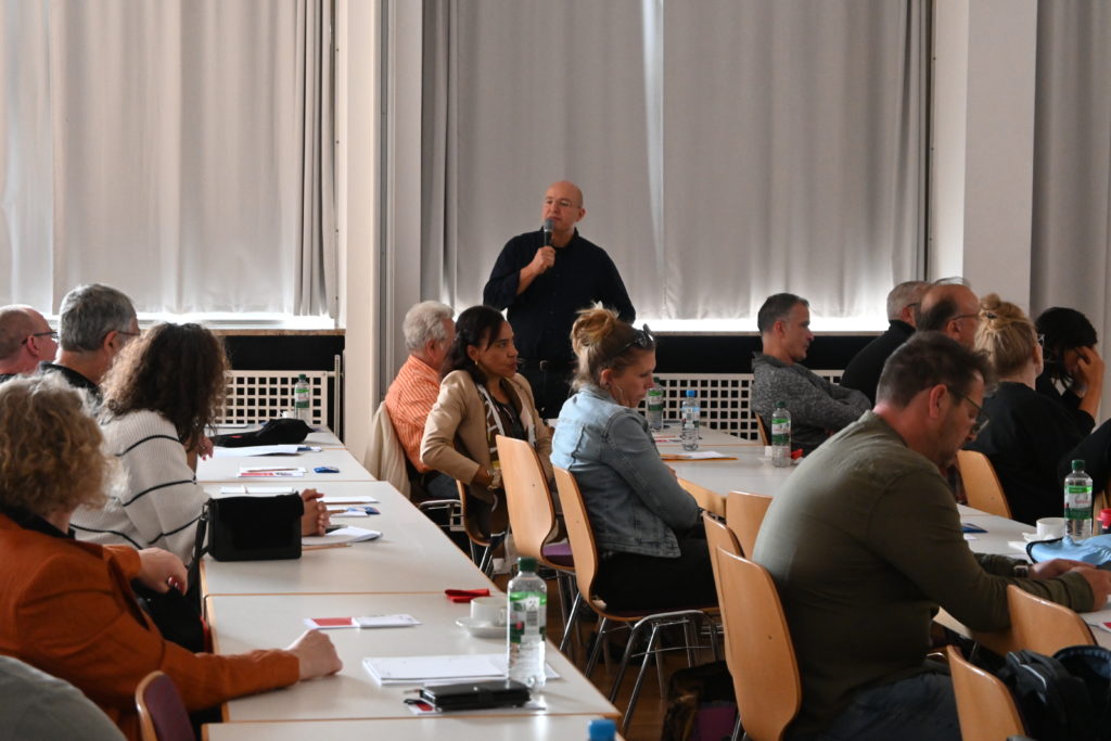 Auf dem Bild sieht man die mit Teilnehmern gut gefüllten Tischreihen auf der Veranstaltung.