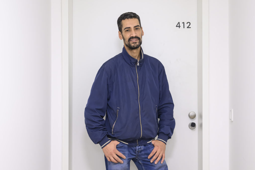 Der Mann mit der blauen Jacke steht vor einer weißen Tür mit der Aufschrift 412.