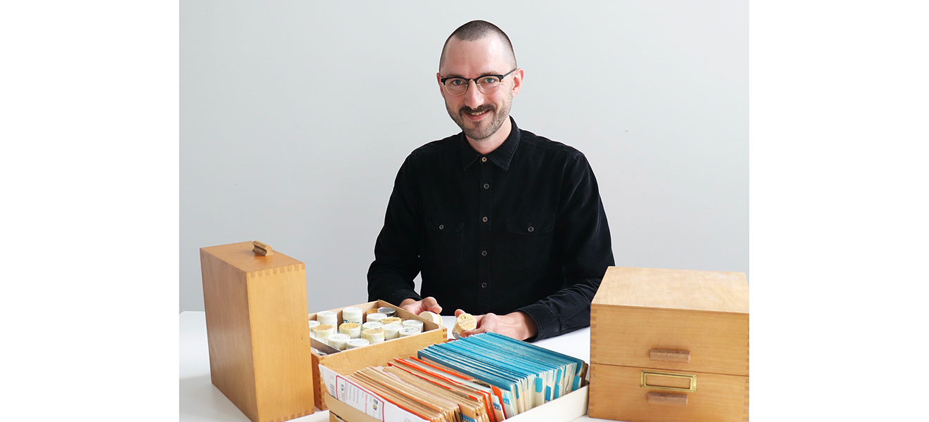 LWV-Archivar Johannes Christof mit dem Fotobestand aus den Gründungsjahren des LWV Hessen (alle Fotos: De Filippo) LWV-Archivar Johannes Christof am Tisch hinter drei Karteikästen sitzend. Er schaut in die Kamera, in den Händen zwei Dosen mit Negativen.