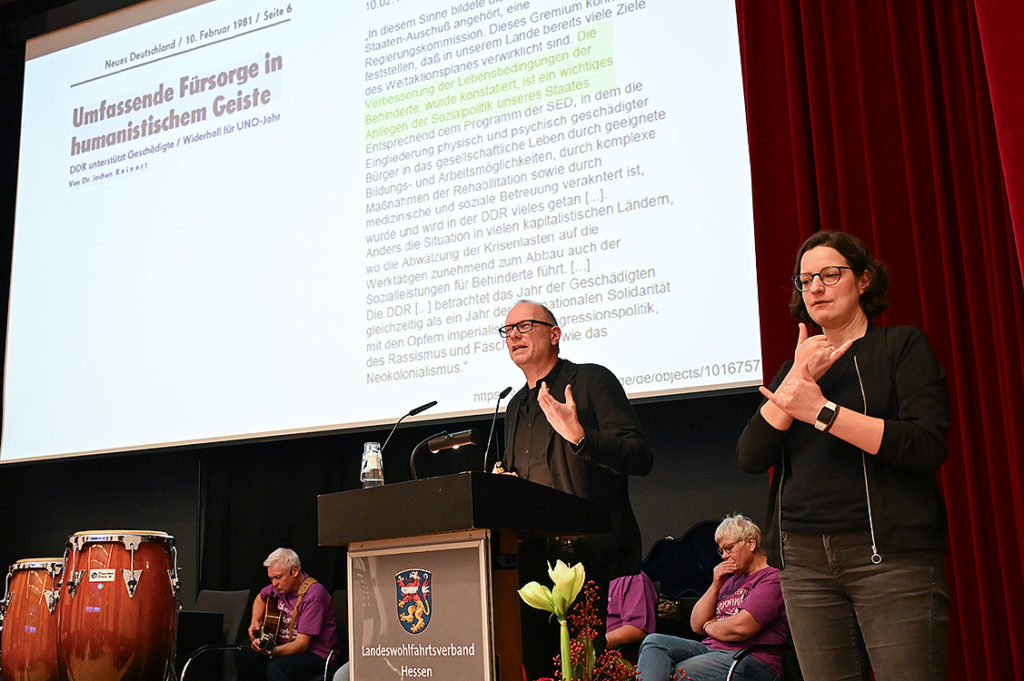 Ein Mann mittleren Alters mit einer Brille hält am Pult engagiert einen Vortrag.