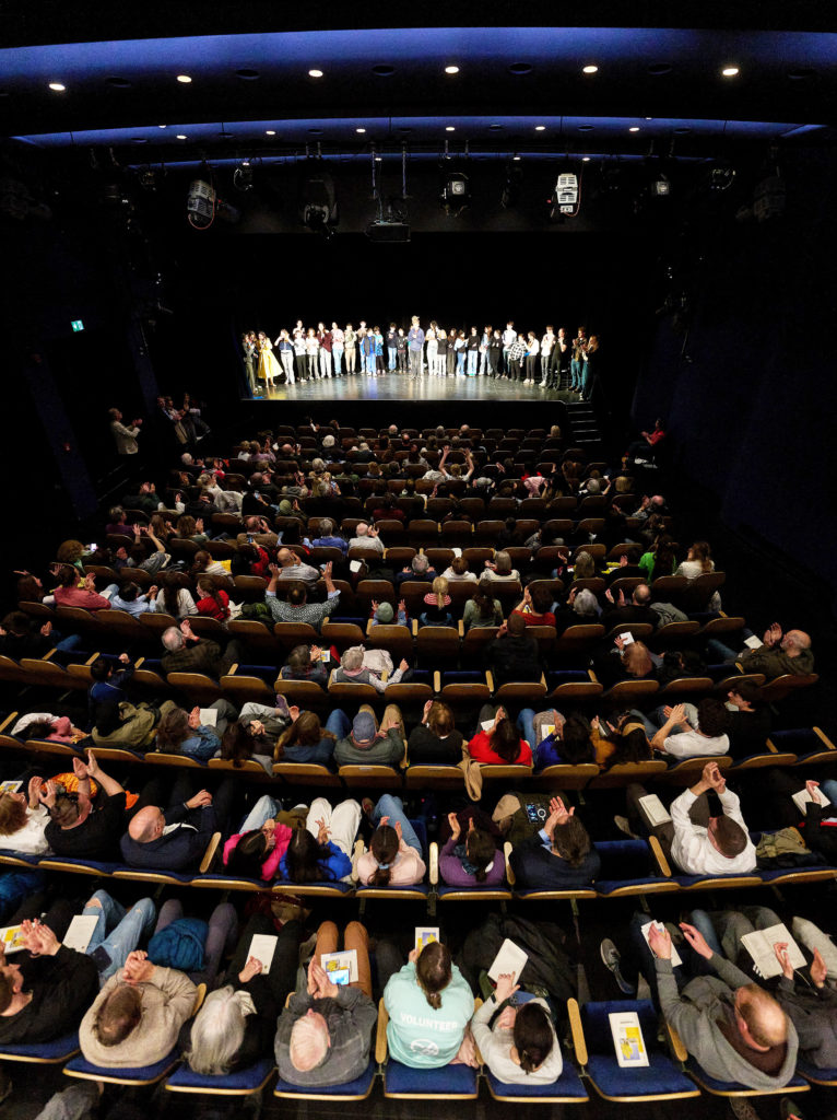 Die Fotografie zeigt das bis auf den letzten Platz gefüllte Theater.