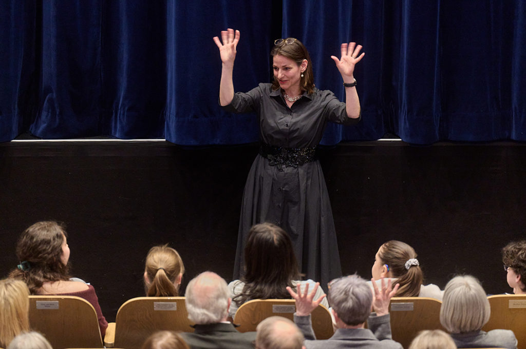 Eine Frau im schwarzen Kleid und mit schwarzen Haaren macht vor Publikum Gebärdensprache. 