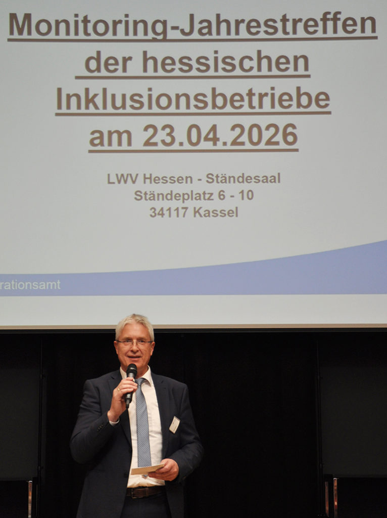 Ein Mann mit Mikriphon steht vor einer Leinwand