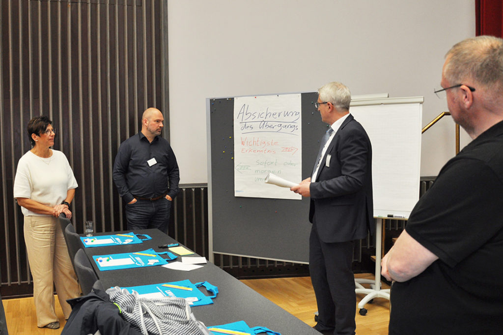 Eine Frau und drei Männer stehen um ein Flipchart herum und reden.