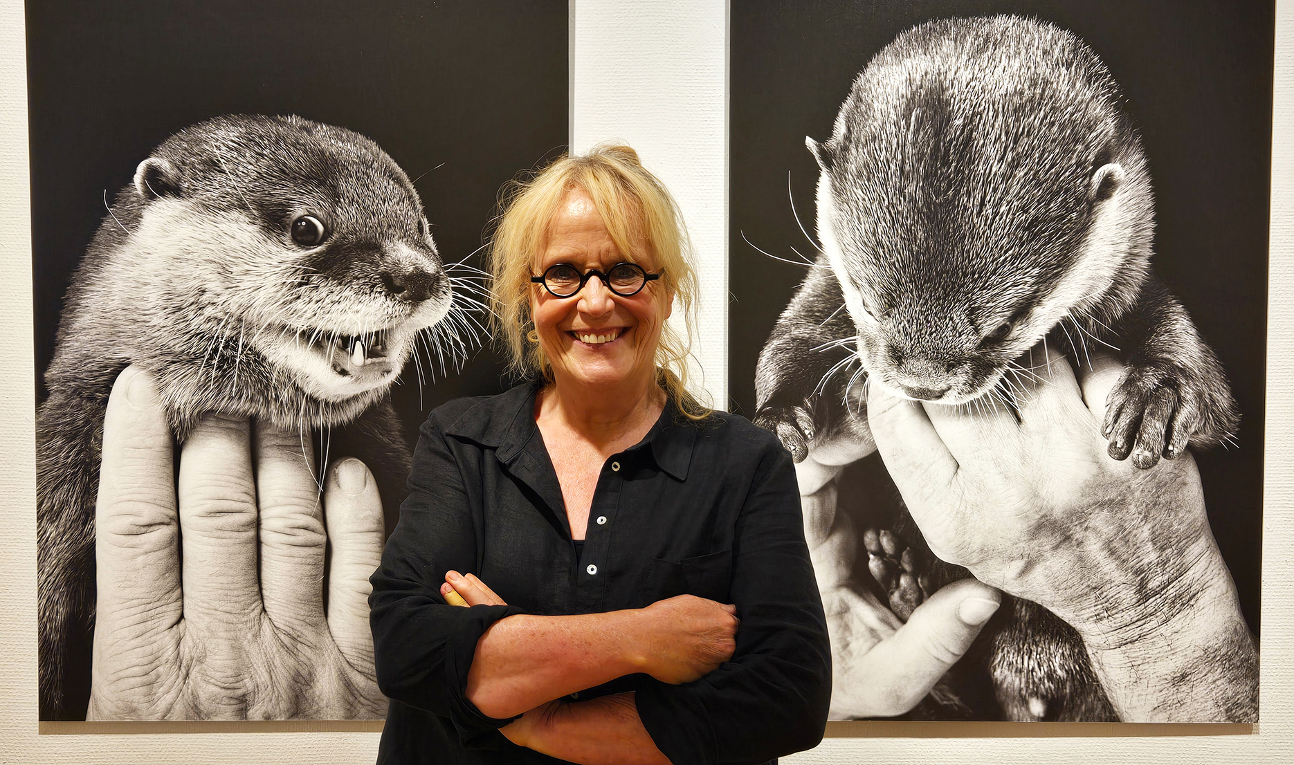 Fotografin Ruth Marcus steht vor einem ihrer Schwarz-Weiß-Fotos in der Ausstellung. Das Foto zeigt zwei Mal den Kurzkrallenotter Nemo auf den Händen des Zoodirektors.